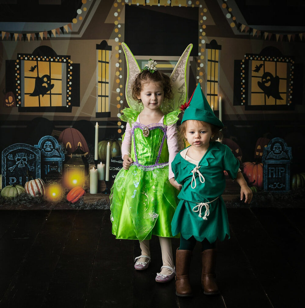 Two toddler girls wearing costumes of fairies and Peter Pan, holding hands for a milestone session in Camden, New Jersey.