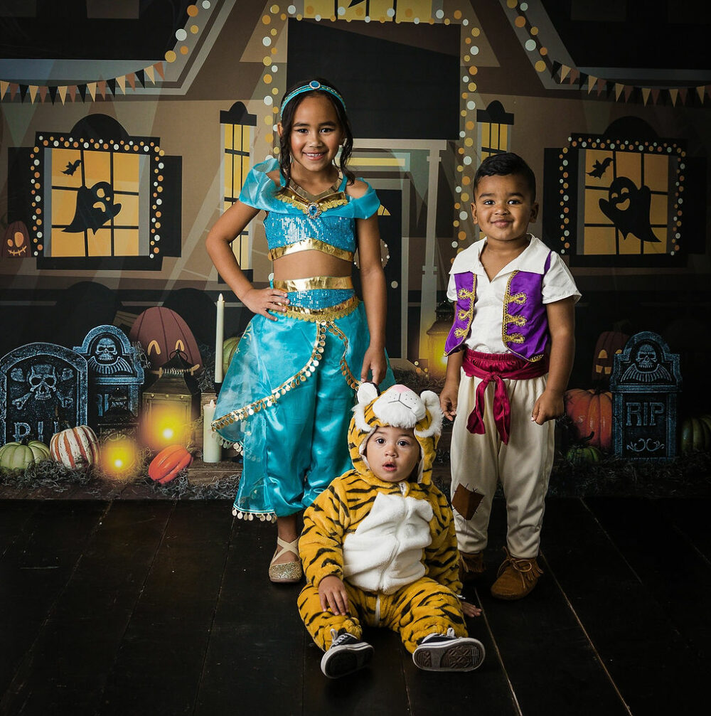 A portrait of three toddlers, a girl wearing a princess costume and a toddler boy wearing Disney character outfit and a baby wearing a lions costume for their monthly milestones session in Eastampton, New Jersey.