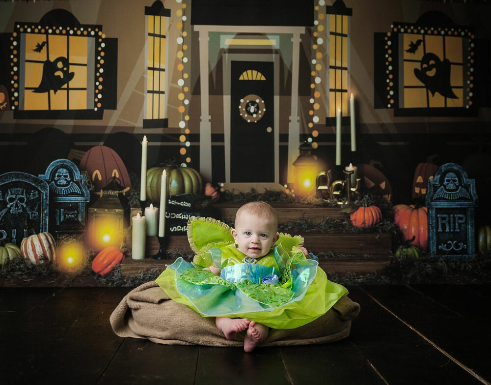 Infant sitting on newborn photography prop smiling at camera for a halloween mini session in Burlington, New Jersey.