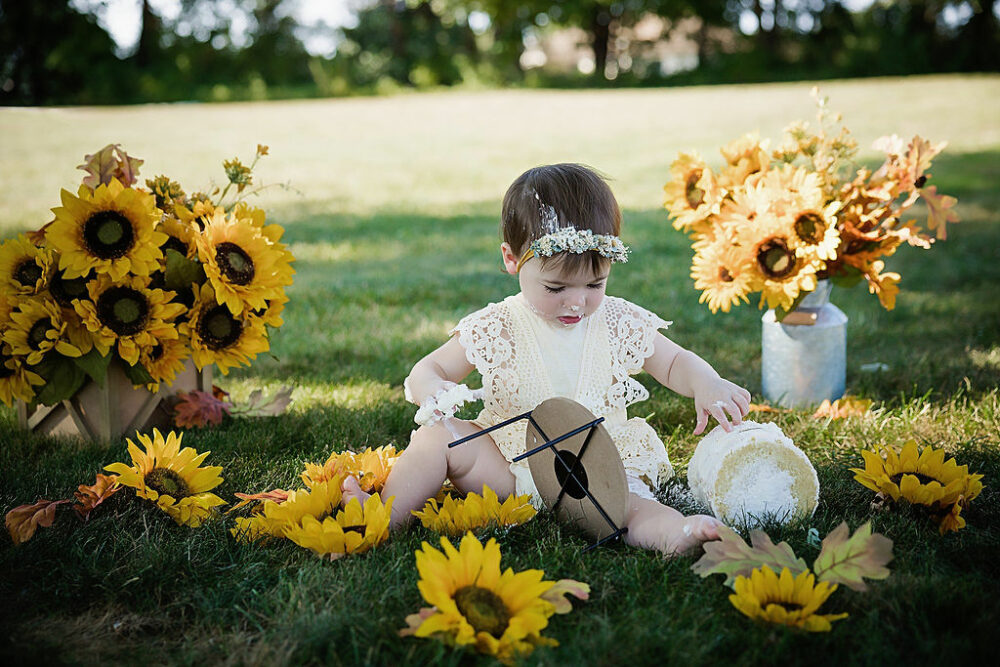 Young girl sitting outdoors adorned with flowers eating a cake first birthday session in Southampton, New Jersey.