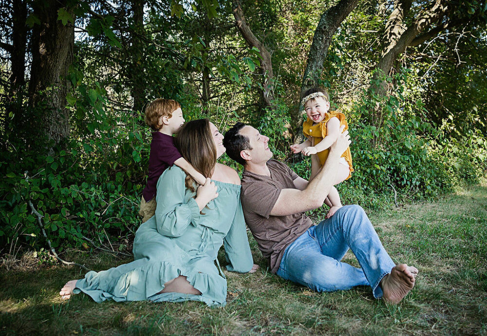 Family portrait of man and woman sitting on ground, outdoors playing with their two kids for a cake smash photo session in Mount Laurel, New Jersey.