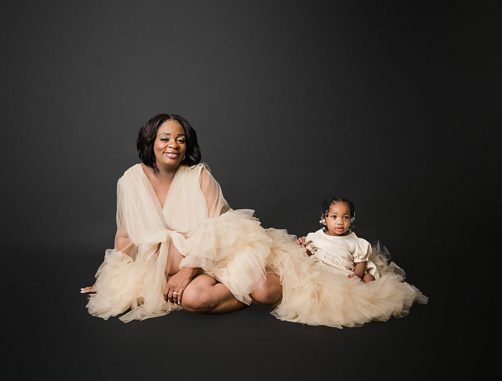 Family portrait of a woman sitting next to her daughter, wearing glamorous down for her professional, maternity photos taken in Marlton, New Jersey.