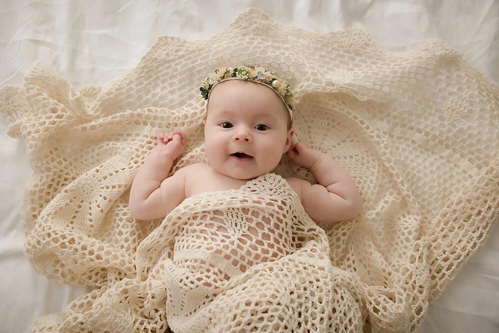 Infant girl laying on a textured blanket wearing headband and smiling at the camera for her Bo ho mommy and me session taken in Southampton, New Jersey.