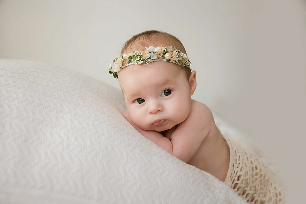 A infant girl resting on her tummy looking to the side wearing headband for her professional photo shoot taken during her Boho mommy and me session taken in Marlton, New Jersey.