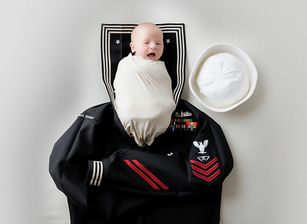 Newborn boy in swaddle, laying on top of his father’s military uniform taken during his Navy newborn session taken in Fort Dix, New Jersey.