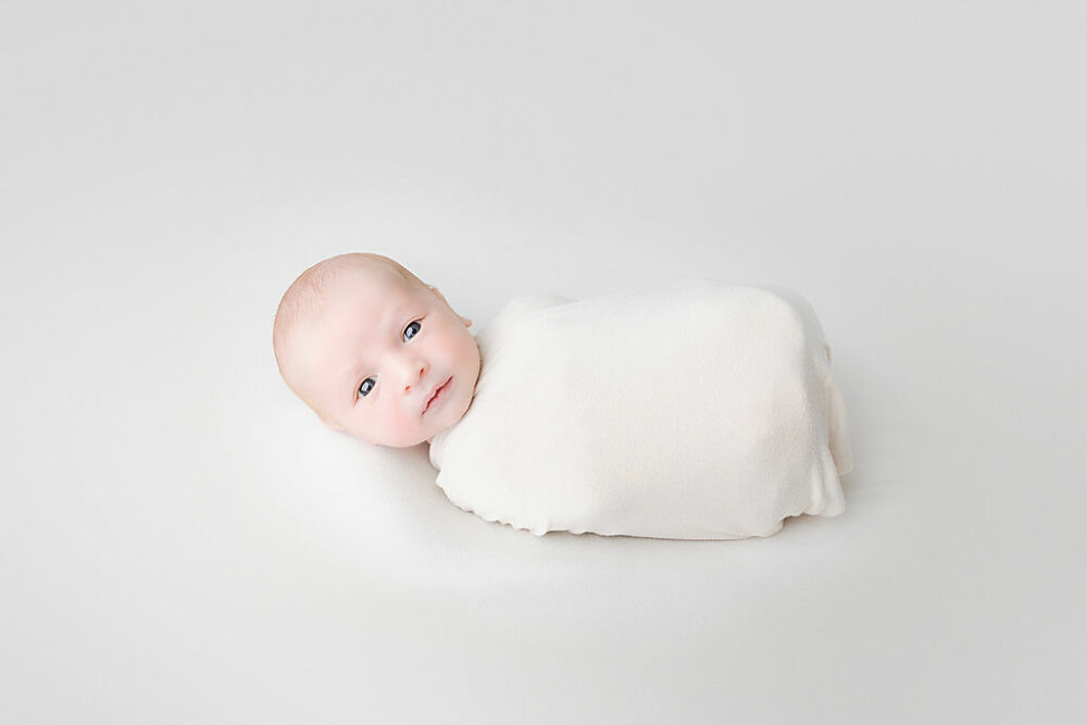An infant boy looking at camera and swaddled taken during his baby photography session in Browns Mills, New Jersey.