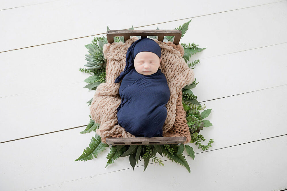 An infant swaddled and wearing matching hat, sleeping on textured blanket on top of crib, photography prop for his first baby photoshoot taken in Camden, New Jersey.