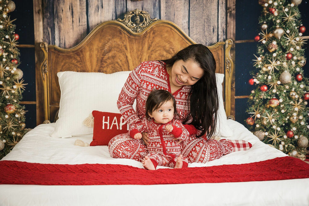 A mother and her toddler son sitting on bed photography prop wearing matching pajamas for their holiday pictures taken in studio in Freehold, New Jersey.