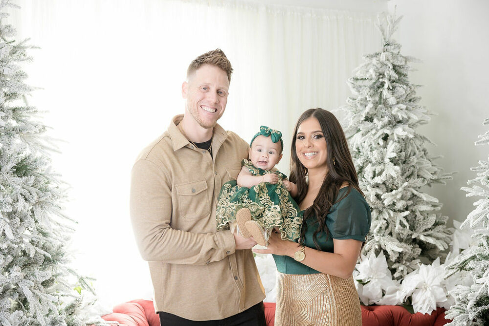 Man and woman smiling at camera as they both hold their daughter, wearing matching outfits for their Christmas pictures taken in Crosswicks, New Jersey.