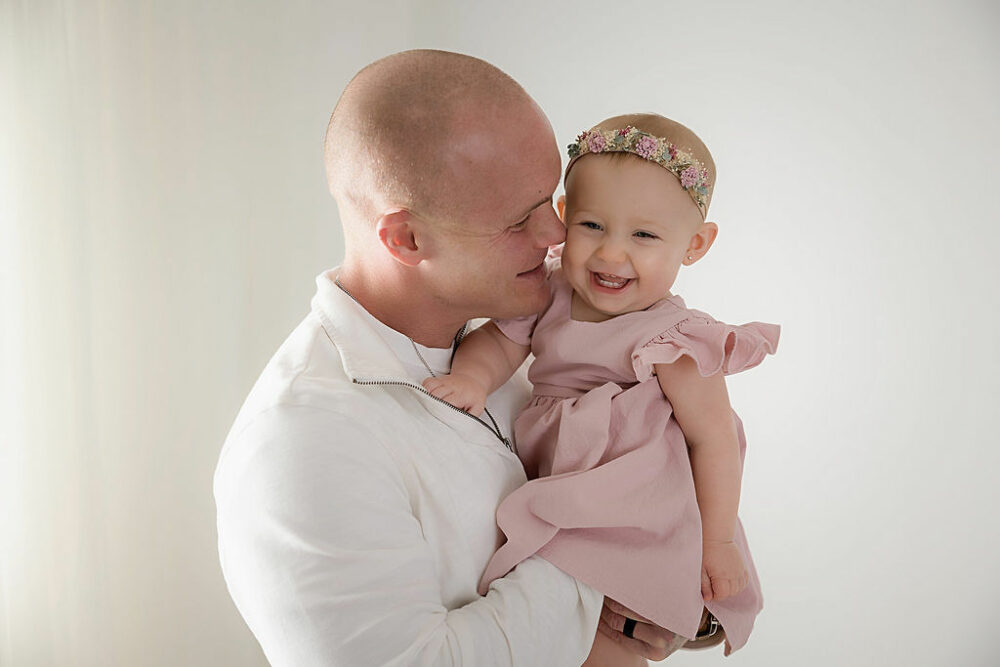 Portrait of a father holding his daughter and both smiling taken during her snowflake first birthday session in Burlington, New Jersey.