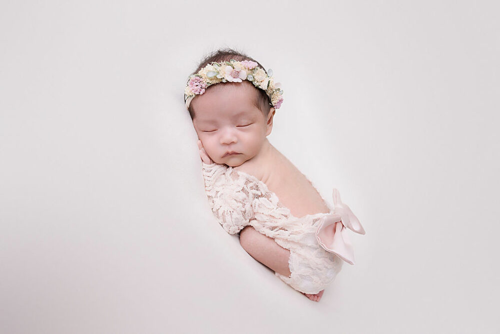 Profile view of a newborn girl sleeping on her tummy wearing infant outfit and headband for her pink in-home newborn session in Cherry Hill, New Jersey.