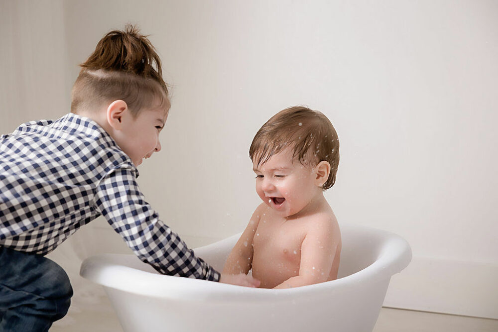Sibling portrait of a toddler boy playing with his infant brother as a splash water and laugh together for his baby milestones first year session in Pemberton, New Jersey.