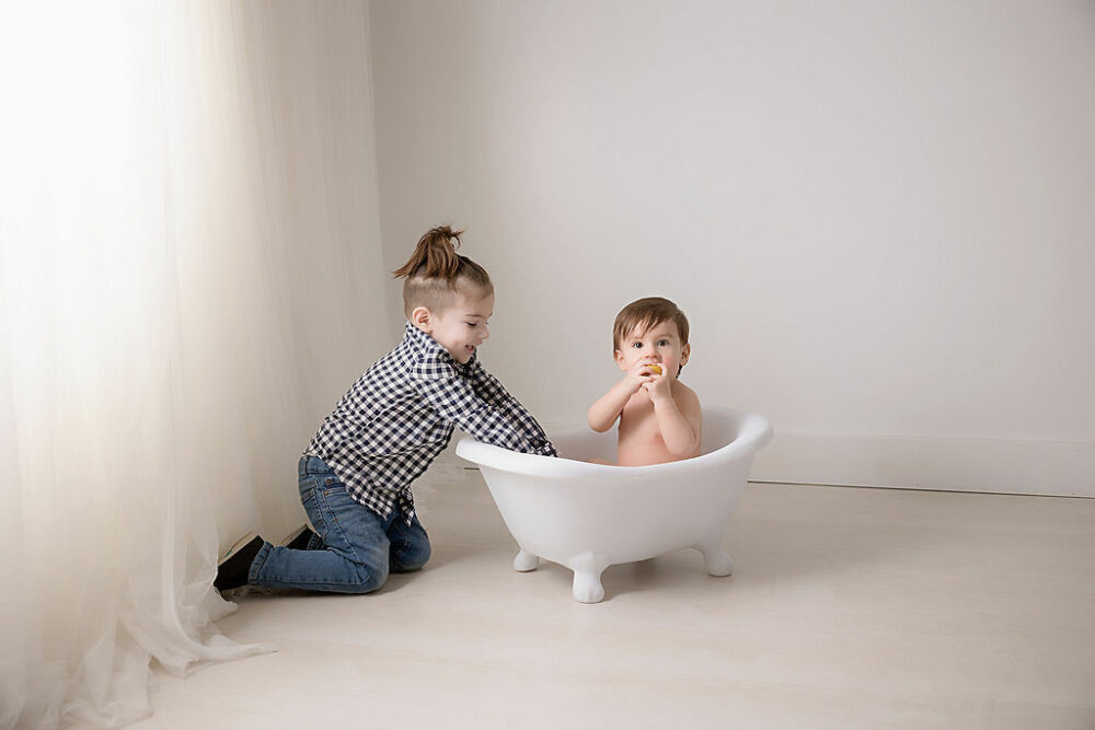 Sibling portrait of two boys, playing and splashing water in tiny tub for a baby development photography session taken in Eastampton, New Jersey.
