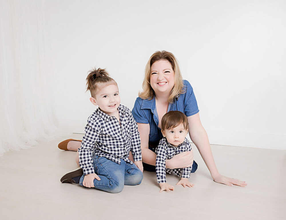 A woman sitting on the floor along with her two sons, who are wearing matching shirts and denim for his cowboy first birthday session in Cherry Hill, New Jersey.