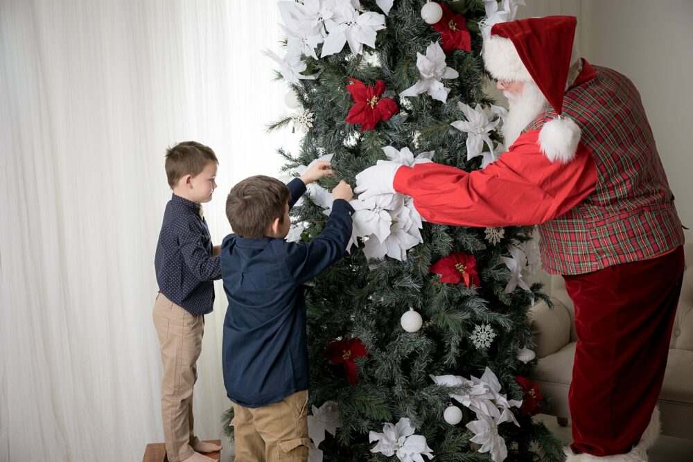 Santa helping a boy put on decorations on a christmas tree