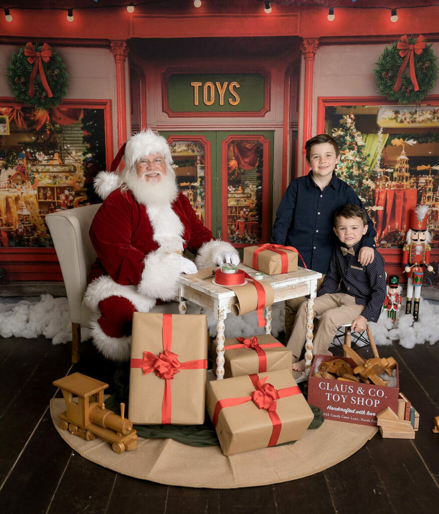 A man dressed as Santa sitting and posing with two boys in photography set for their Santa mini session in Mount Holly, New Jersey.