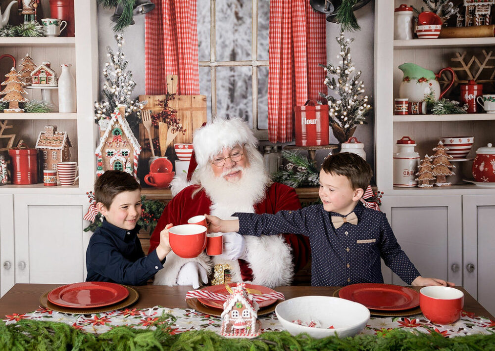 A man dressed in holiday outfit toasting hot cocoa with two toddler brothers in holiday set for Santa mini sessions in Cherry Hill, New JErsey.