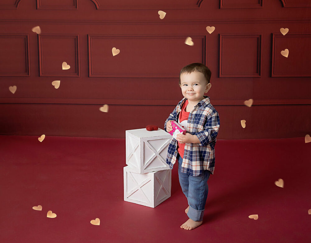 Toddler boy holding candy box and smiling for his in studio Valentine’s Day mini session in Pemberton, New Jersey.