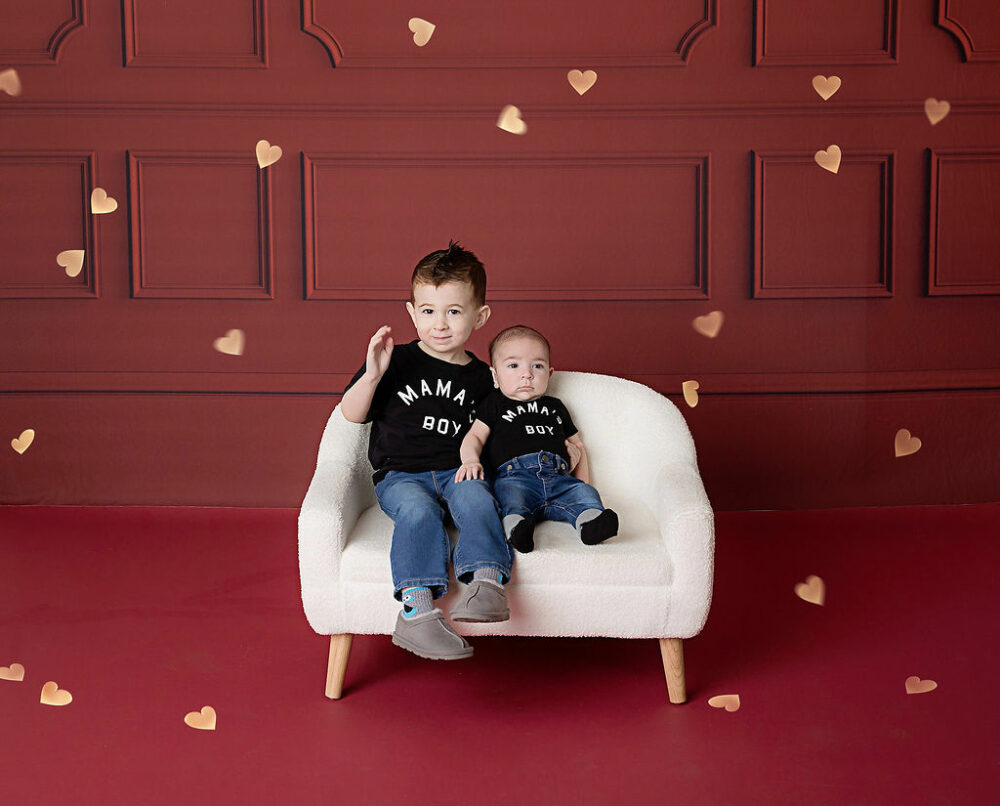 Two siblings sitting on bench photography prop waving and wearing matching outfits for their VDay Mini Session in Southampton, New Jersey.
