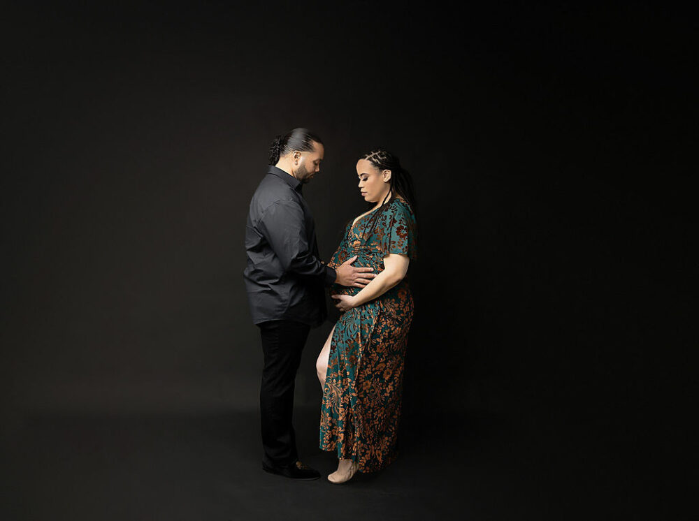 Glamorous, maternity portraits of a man and woman facing each other, and holding her belly for her pregnancy photography session in Hamilton, New Jersey.