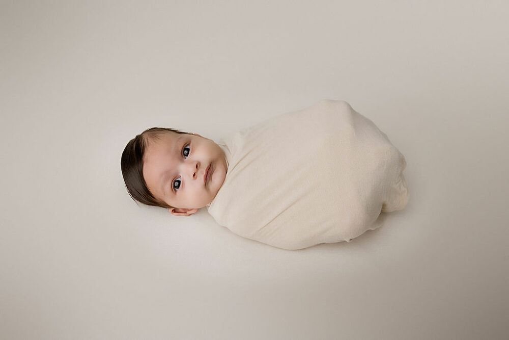 An infant wrapped and laying on his back against a light backdrop for his Newborn photography session in Southampton, New Jersey.