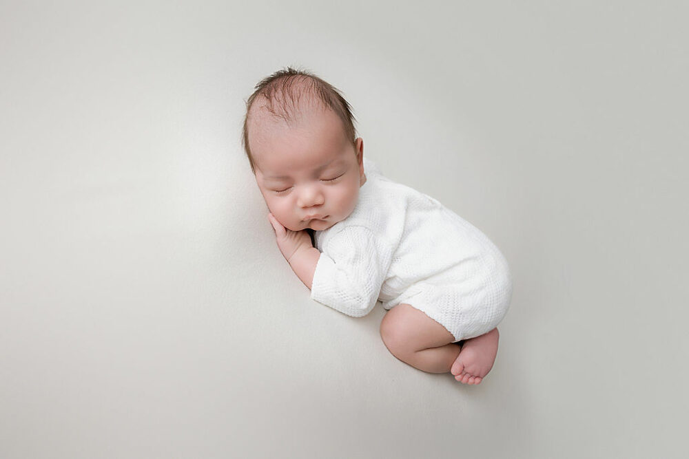 An infant boy sleeping on his tummy, wearing onesie, on bean bag photography prop four his professional baby photos in Hamilton, New Jersey.