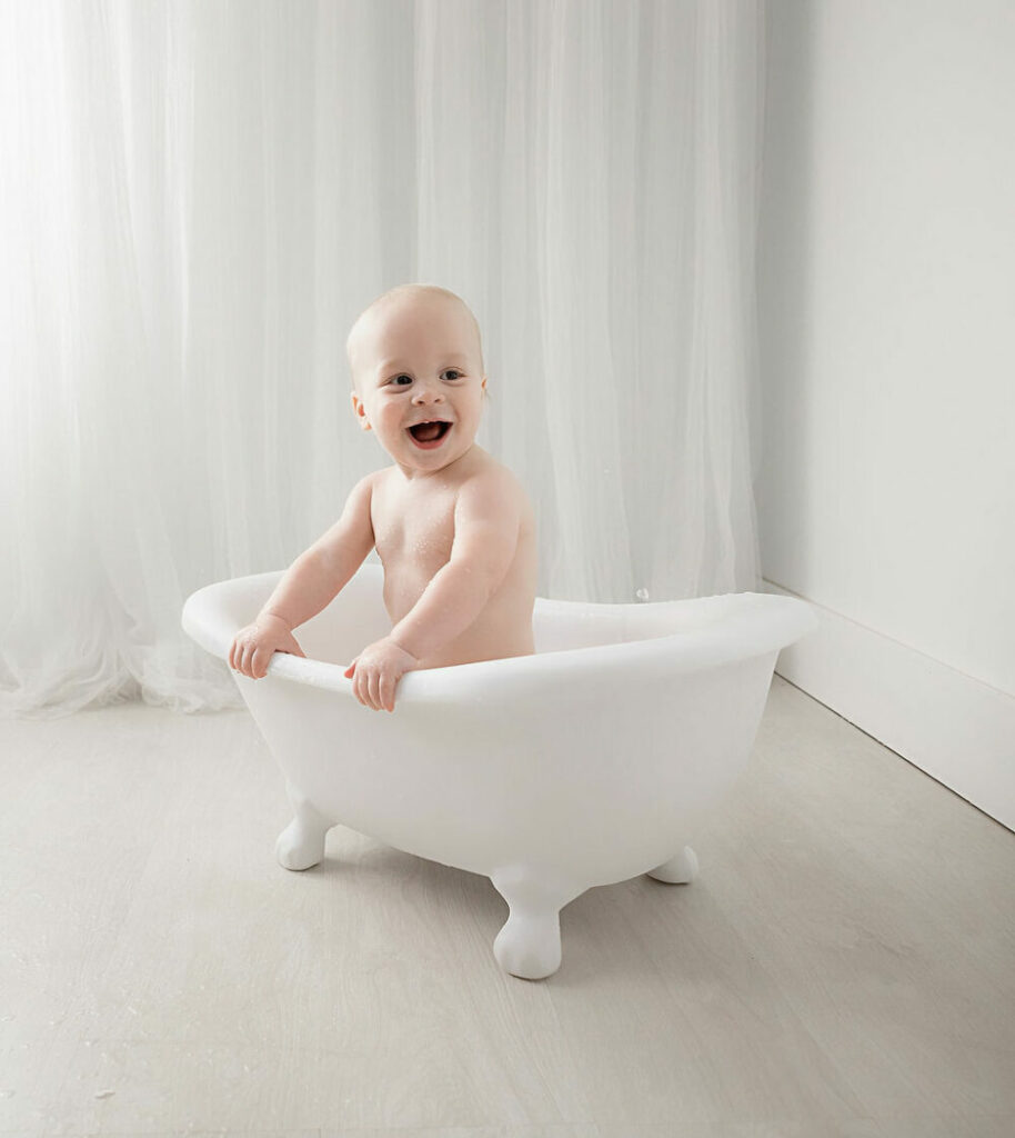 A toddler smiling as he sit in tiny bathtub for his professional birthday images taken in Eastampton, New Jersey.
