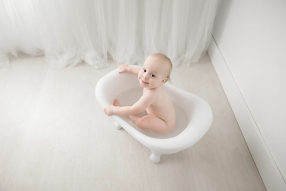 Aerial portrait of a boy sitting in tiny bathtub and playing taken during his minimalist first birthday session in Hamilton, New Jersey.