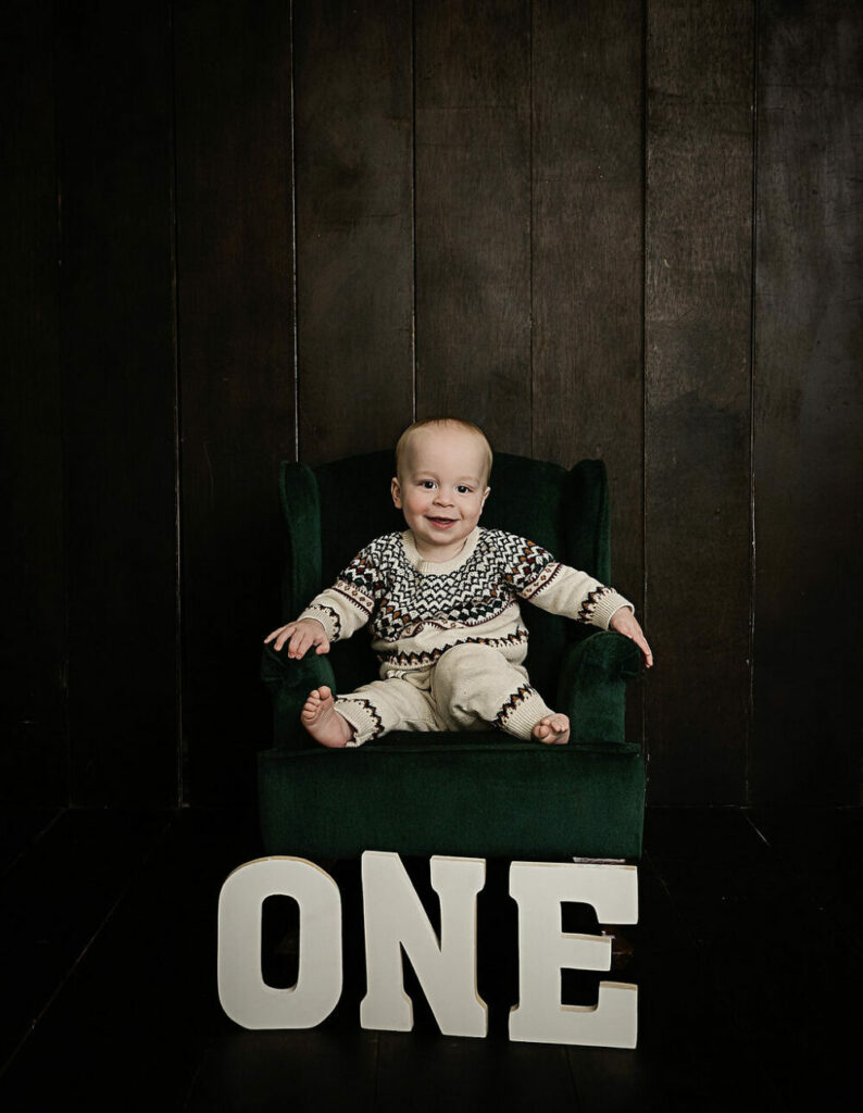 Toddler boy sitting on little couch with photography props spelling out the word one for his minimalist first birthday session in medford, New Jersey.