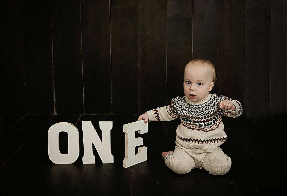 A toddler boy sitting on ground while holding the letter E for his first birthday party themes in Burlington, New Jersey.
