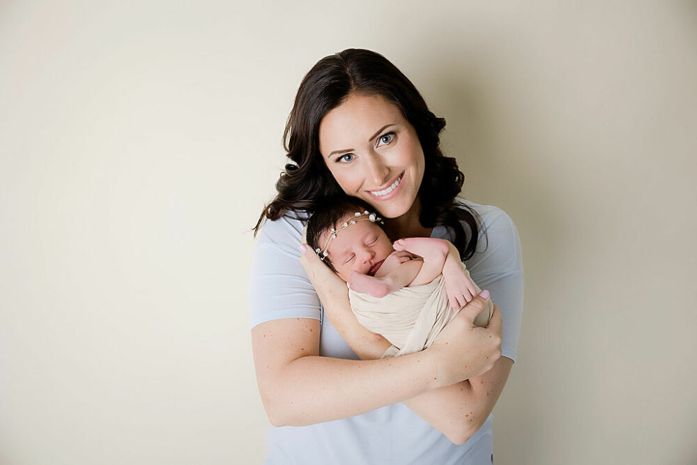 A woman, smiling as she holds her newborn girl in her arms for her professional newborn session in Burlington, New Jersey.