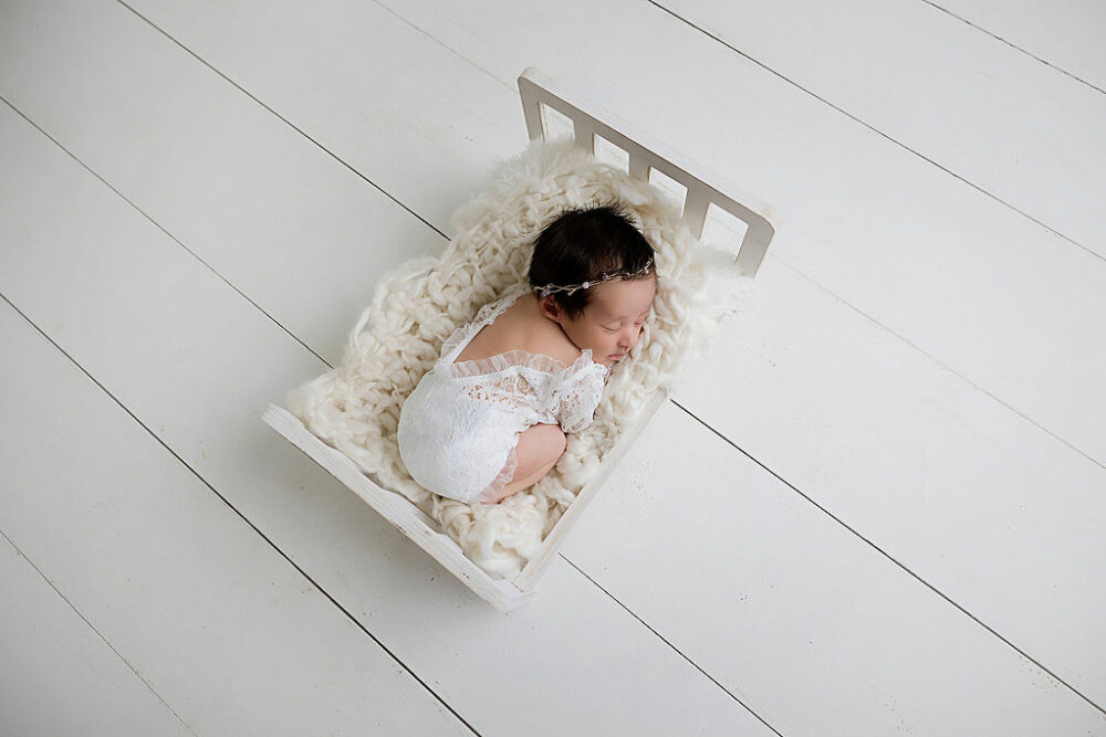 A newborn girl sleeping on her belly on textured, blanket and tiny crib, photography prop for a newborn session in Cherry Hill, New Jersey.