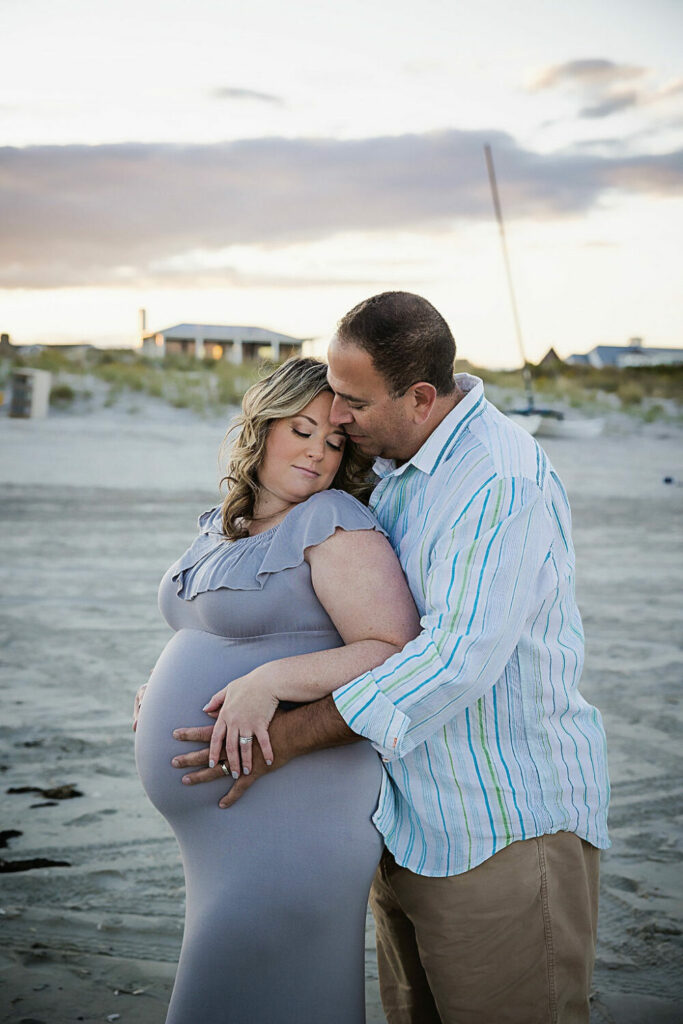 Couple portrait of a man standing behind his pregnant wife holding their belly for a beach maternity session taken in Cape May, NJ.