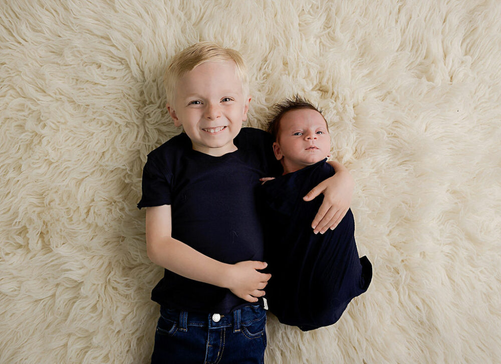 Sibling photography of two brothers laying on ground and posing for their profession newborn portraits in Washington, New Jersey.