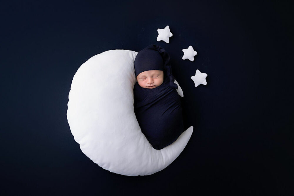 Newborn, baby images of a boy, wrapped and sleeping on moon shaped pillow, adorned with stars, his newborn session in Voorhees, New Jersey.
