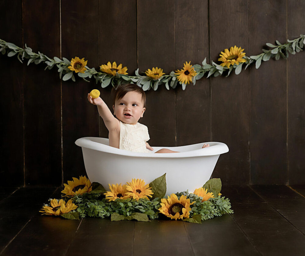 Baby photos portrait photography of a toddler sitting in photography prop bathtub adorned with sunflowers for a first birthday ideas honeybee theme photo shoot in Pemberton, New Jersey.