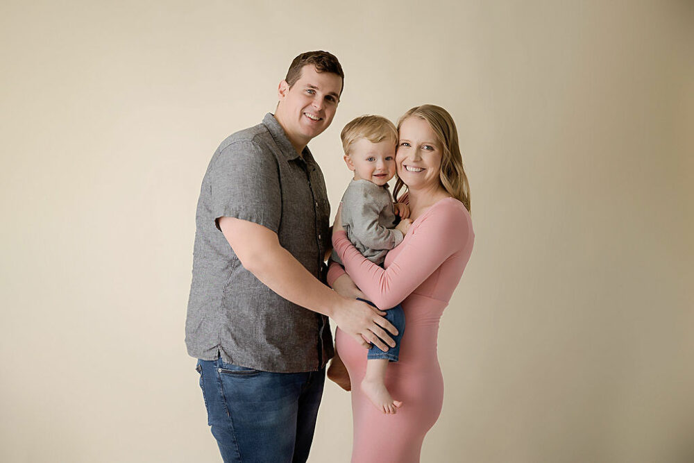 A family portrait of a man and woman, smiling while holding their toddler in between them for maternity session in cherry hill, New Jersey.