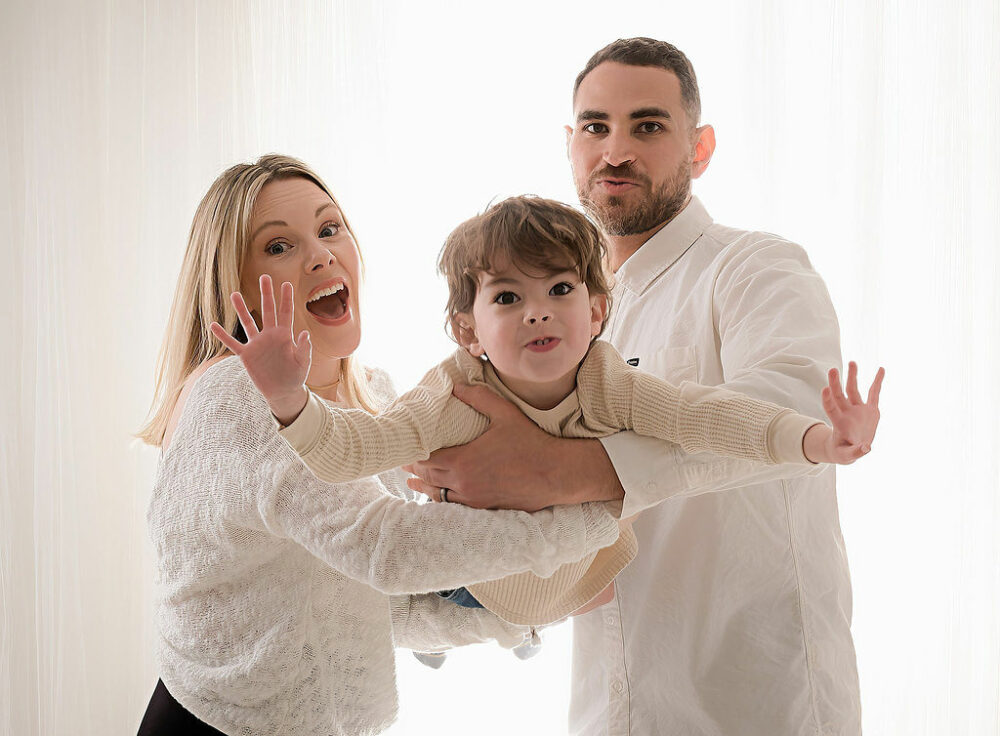 Family group photo of a man and woman carrying their toddler in their arms for their family photo poses taken during their lifestyle session in Hamilton, New Jersey.