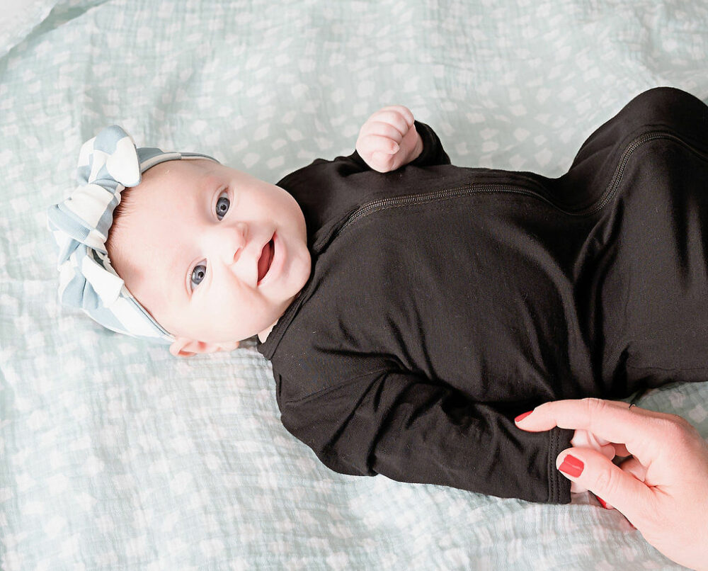 Close up of newborn girl wearing long sleeve onesie and headband smiling for her newborn photography taken in Westampton, New Jersey.