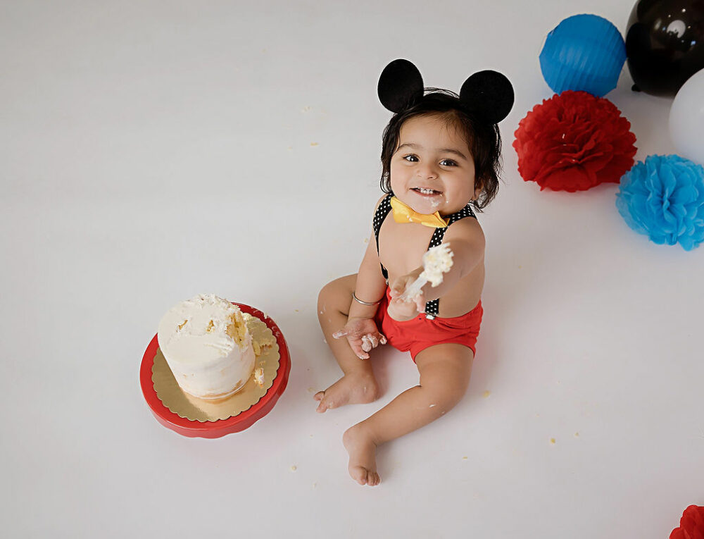 Birthday portrait of a one year old, eating cake, wearing Disney themed outfit for her professional kick smash session in Camden, New Jersey.
