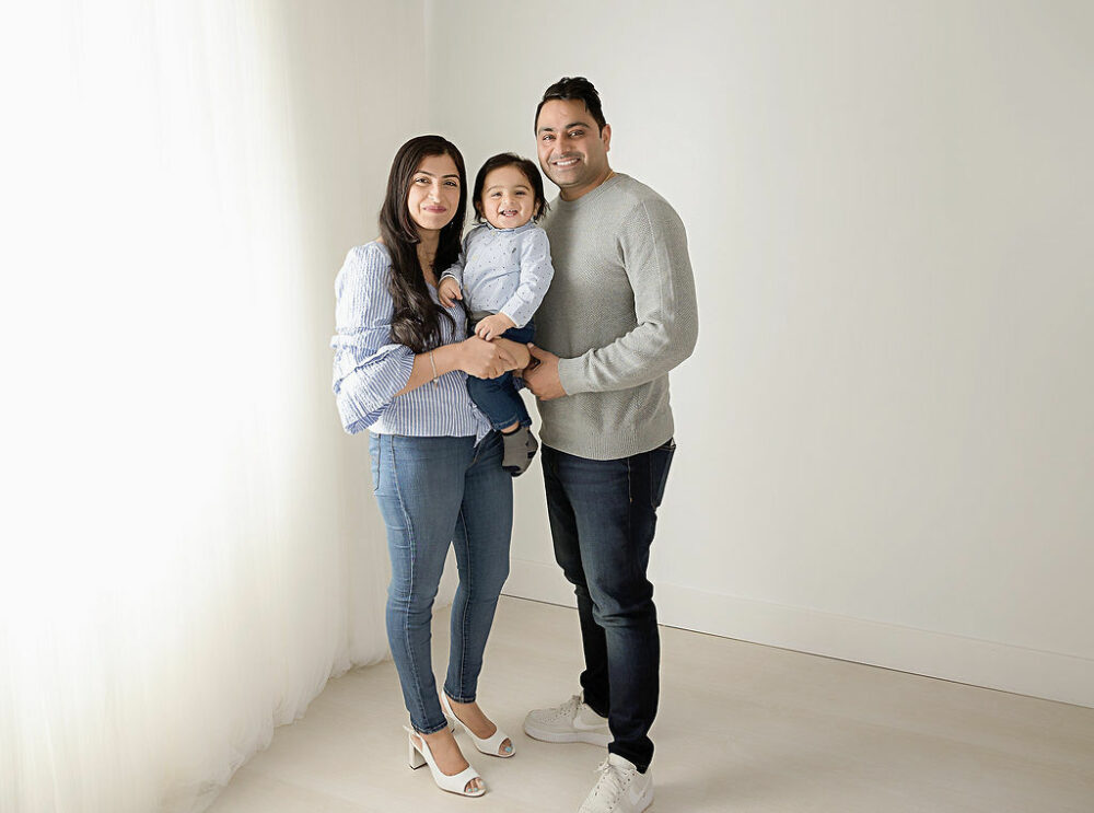 Family photos of a woman and man posing with their one year old and smiling for their professional photographer in Deptford, New Jersey.
