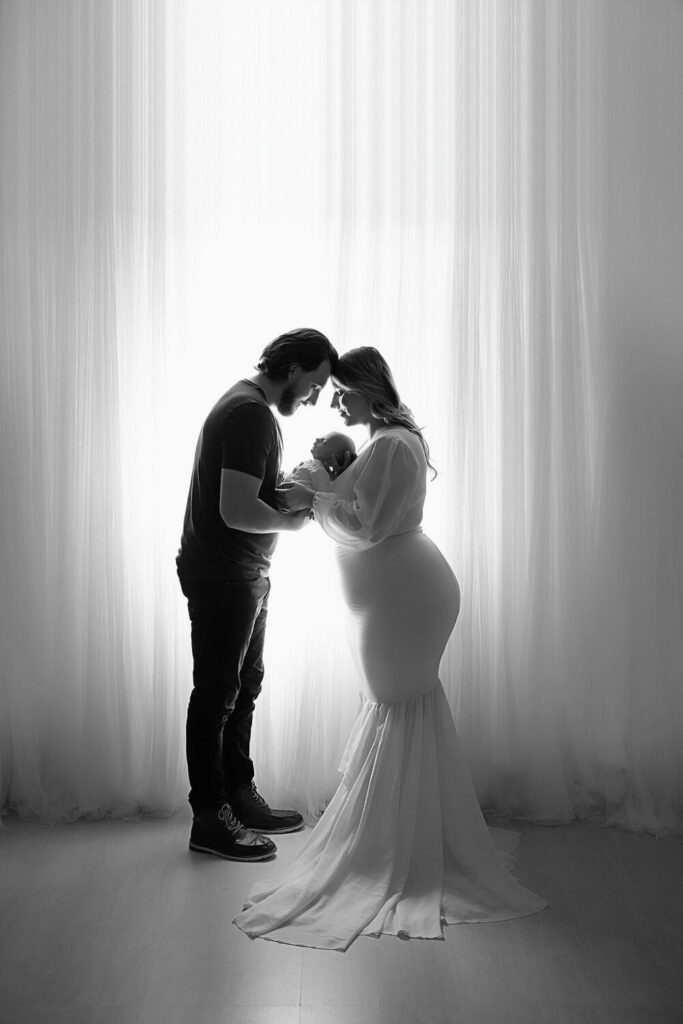 Side-view of a man and woman facing eachother and touching foreheads as they both hold their baby between them for their newborn baby boy photoshoot in Pemberton, New Jersey.