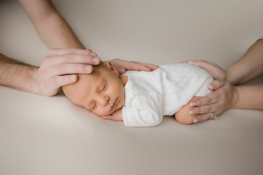 An infant laying on his stomach wearing baby outfit while his parents hold him for a close-up for his baby picture ideas in Medford, New Jersey.
