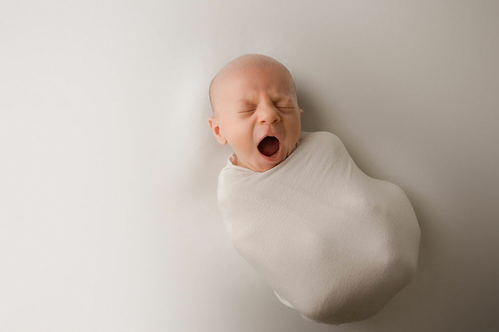 An aerial view of an infant boy, yawning as he is wrapped and laying on back for his professional, baby pics, taken in Warren, New Jersey.