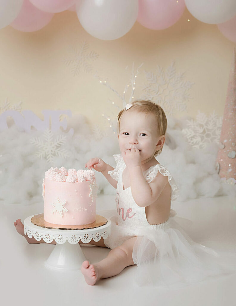 Close up of a toddler girl in pink photography, set wearing cute dress and eating cake for her winter onederland First birthday session in Trenton, New Jersey.