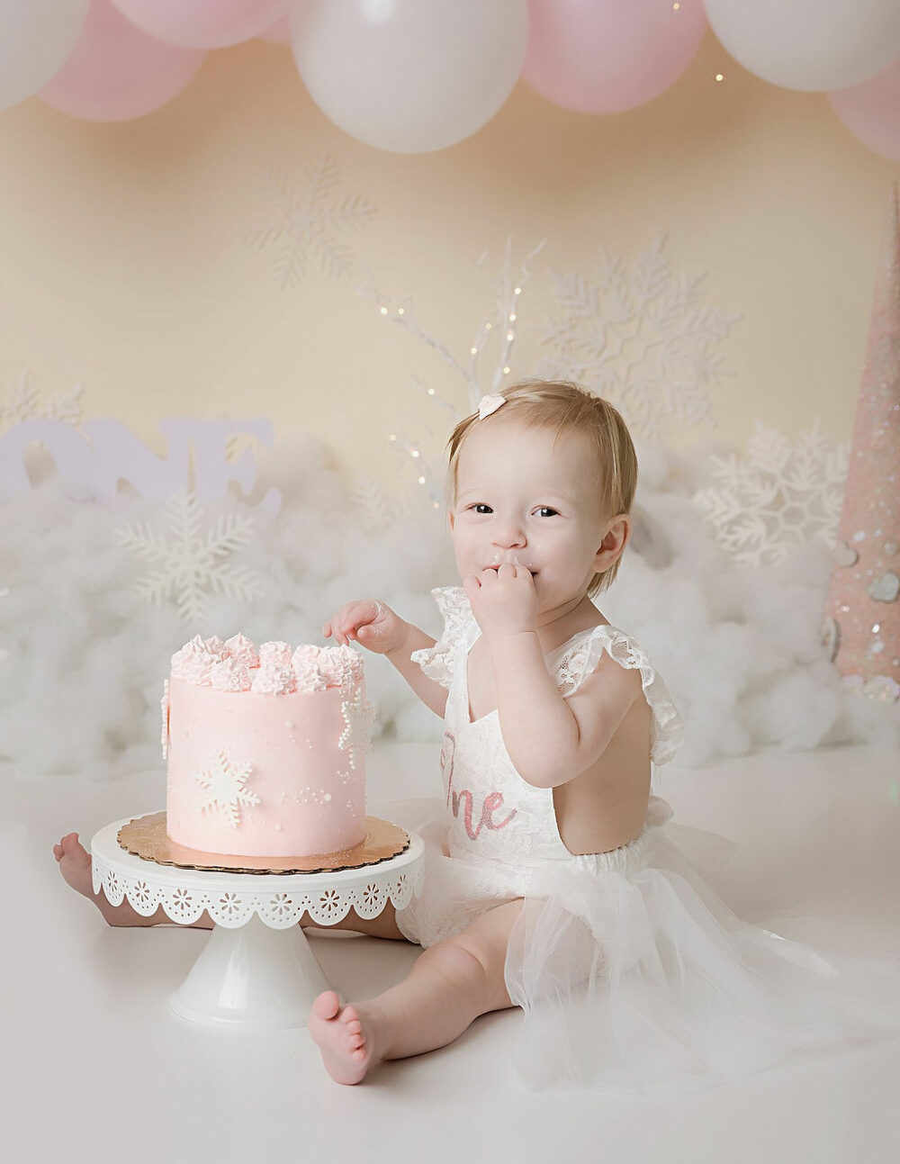 Close up of a toddler girl in pink photography, set wearing cute dress and eating cake for her winter onederland First birthday session in Trenton, New Jersey.