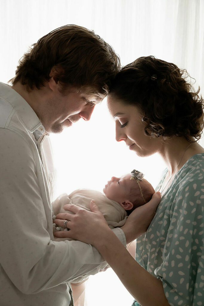 A man and woman facing each other and touching foreheads as a both holder newborn in their hands posing for a beauty and the beast newborn session in Southampton, New Jersey.