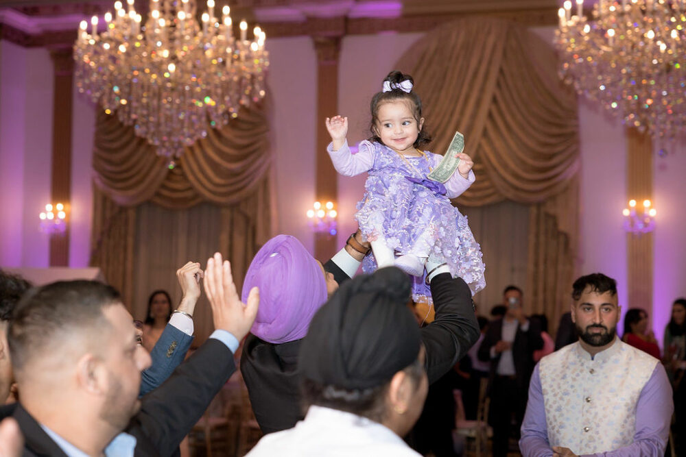 Lifestyle portrait of a man holding up a toddler girl in the air taken during her first birthday party with chandeliers in the background and a grand Manor in Berlin, New Jersey