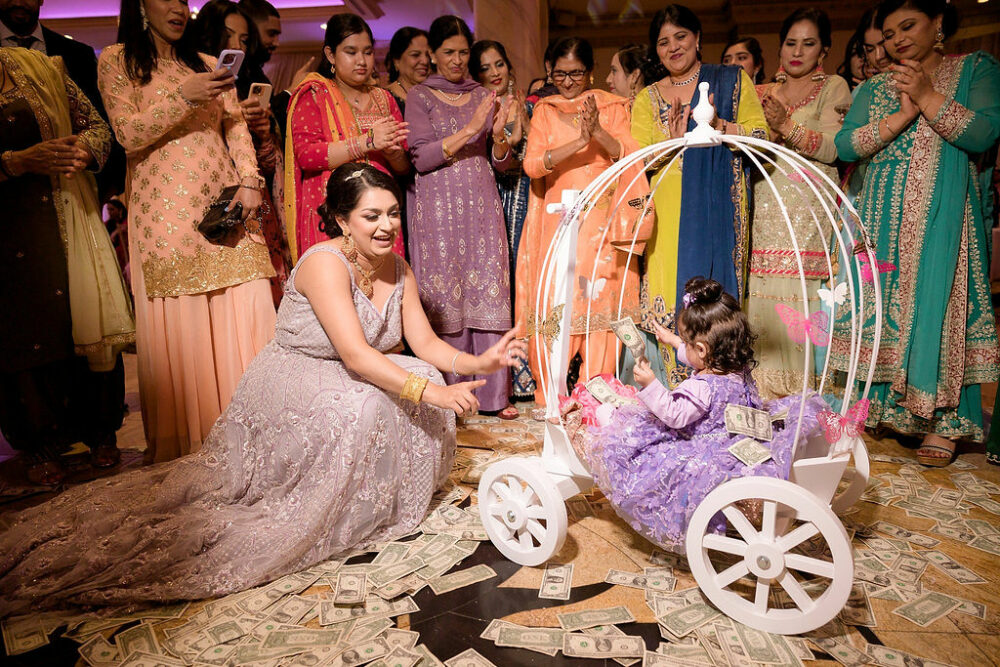 A family on a party dance floor celebrating a toddler during her one year old birthday as she wears cute dress and sitting in a carriage for her when your birthday cake photos in Cherry Hill, New Jersey.