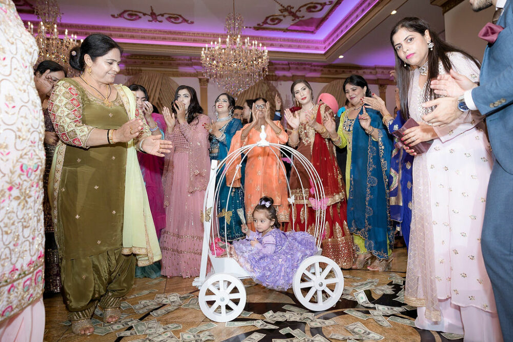 Good photo of a large family dancing on a vent Dancefloor wearing traditional Indian clothing and a toddler in the middle of the dance floor sitting in white carriage in pretty dress for her event birthday photography in Tabernacle, New Jersey.